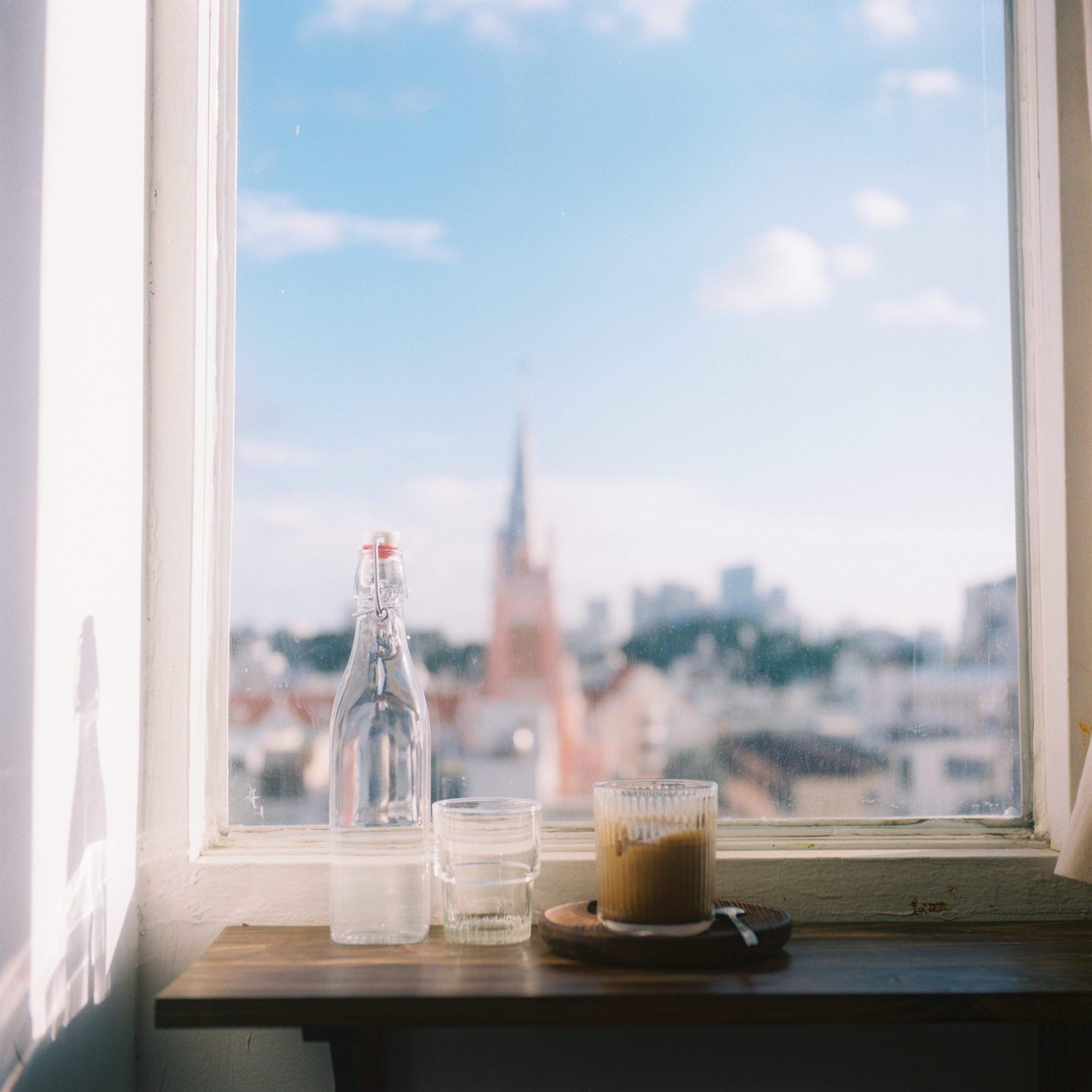 A glass of water on a window sill with a view of a city.