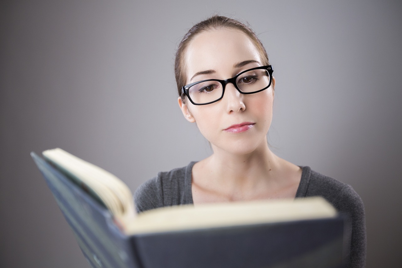 A woman wearing glasses is reading a book.